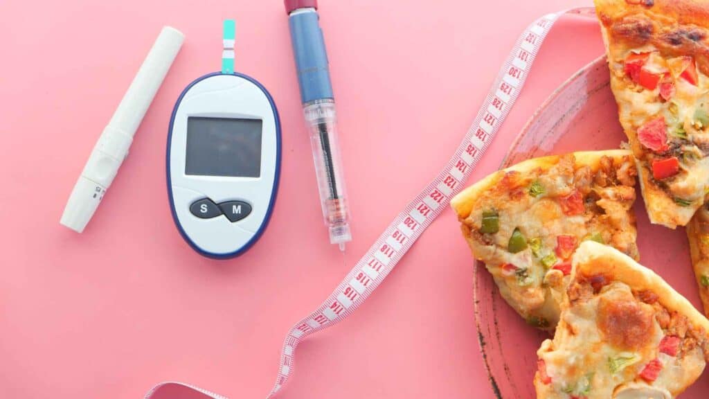 Glucose monitor machine, lancet, measuuring tap, and slices of pizza on a table