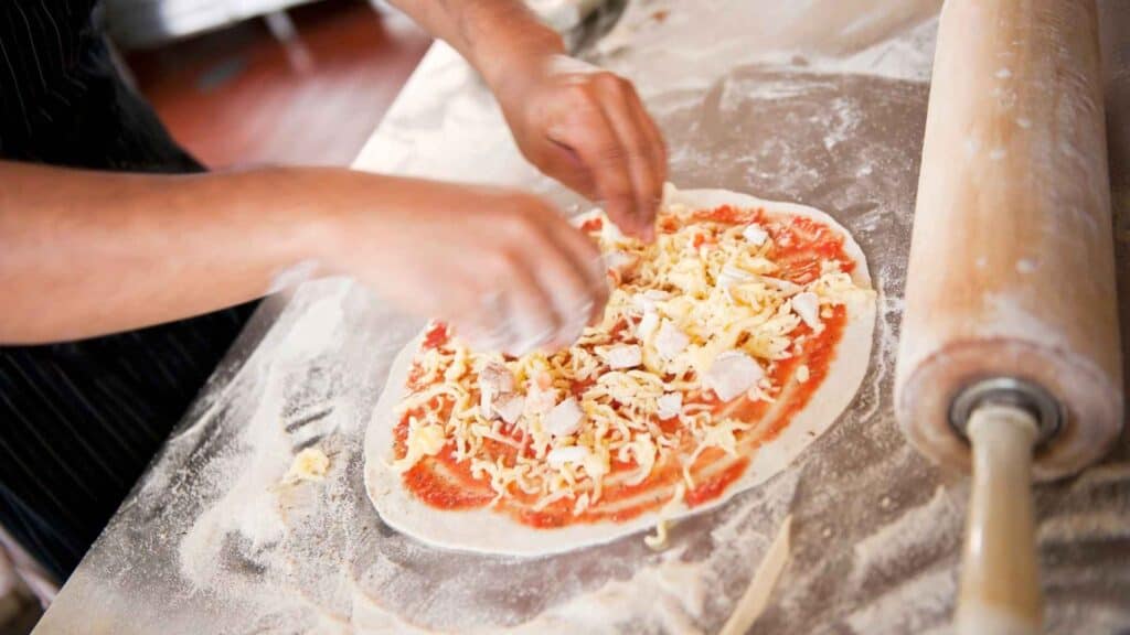 A man topping on thin-crust pizza 