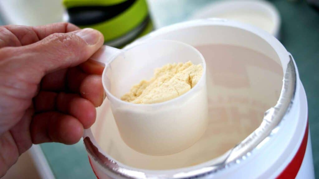 protein jar with a cup full of protein powder in the hand of a person