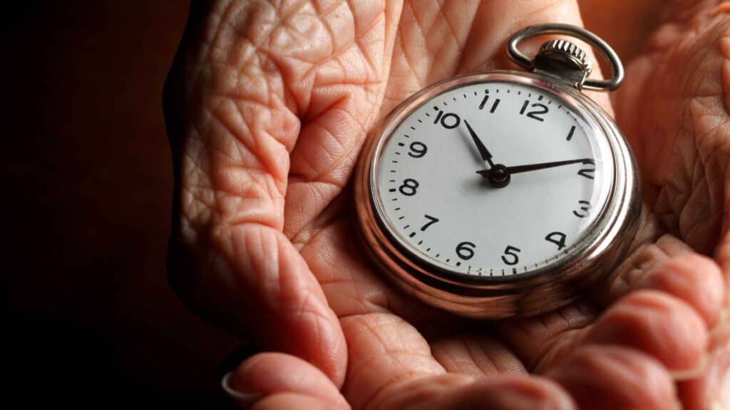 An old man hands with an analogue clock, aging concept