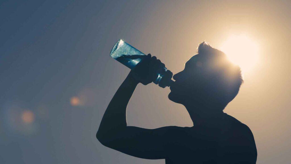 A young man drinking water in strong sun rays